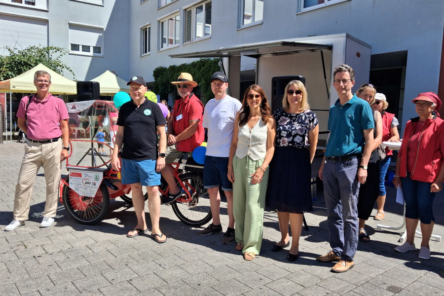 Gruppe von acht Personen steht vor einem offenen Lieferwagen, daneben ein Lastenfahrrad mit bunten Luftballons.